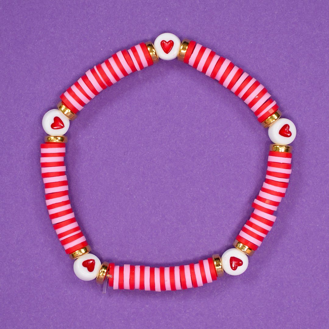 Close up of pink and red beaded bracelet with red hearts on purple background