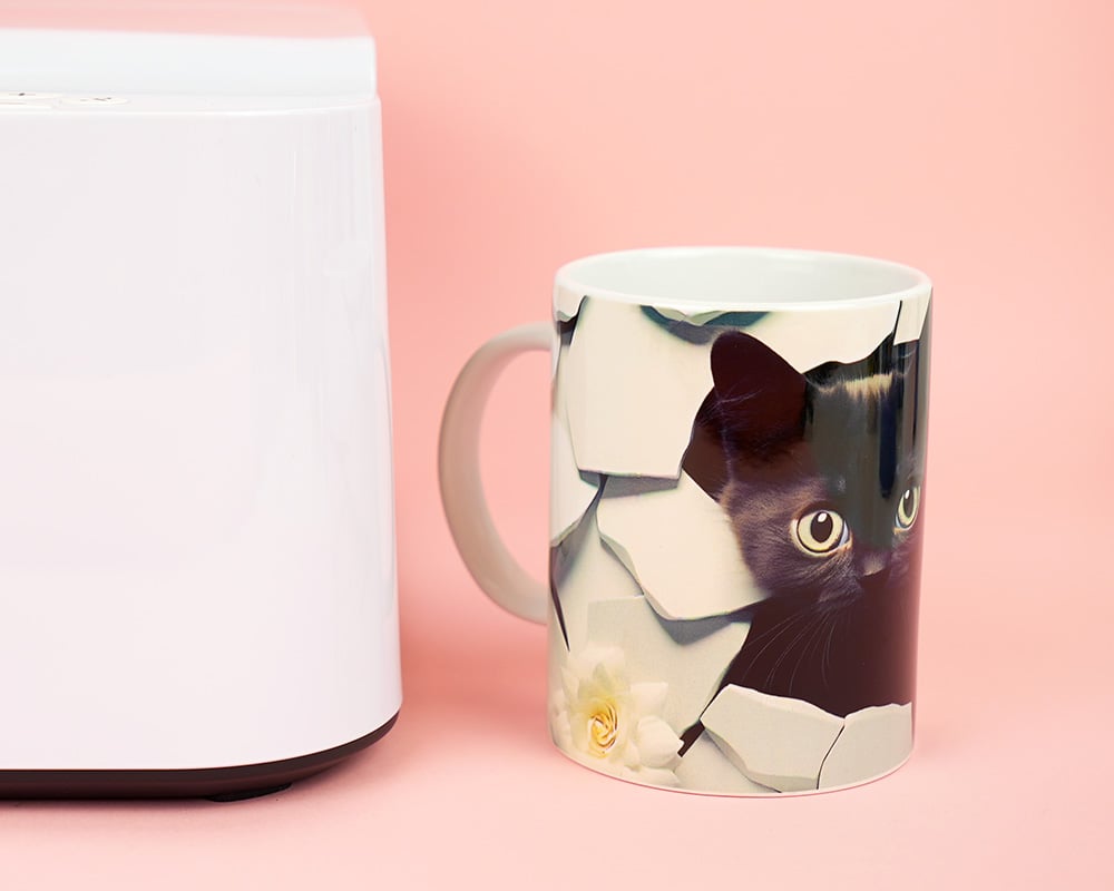 Sublimated cat mug next to the HTVRONT Auto Tumbler Press on pink background