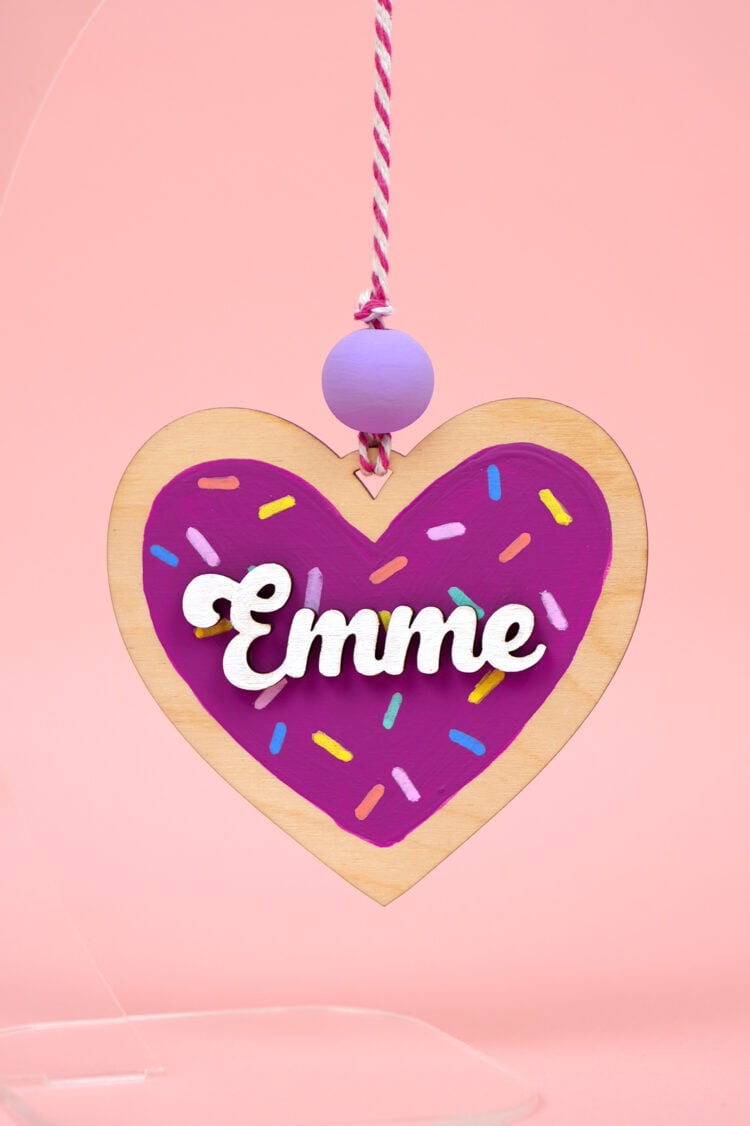 Close up of "Emme" heart cookie ornament on pink background
