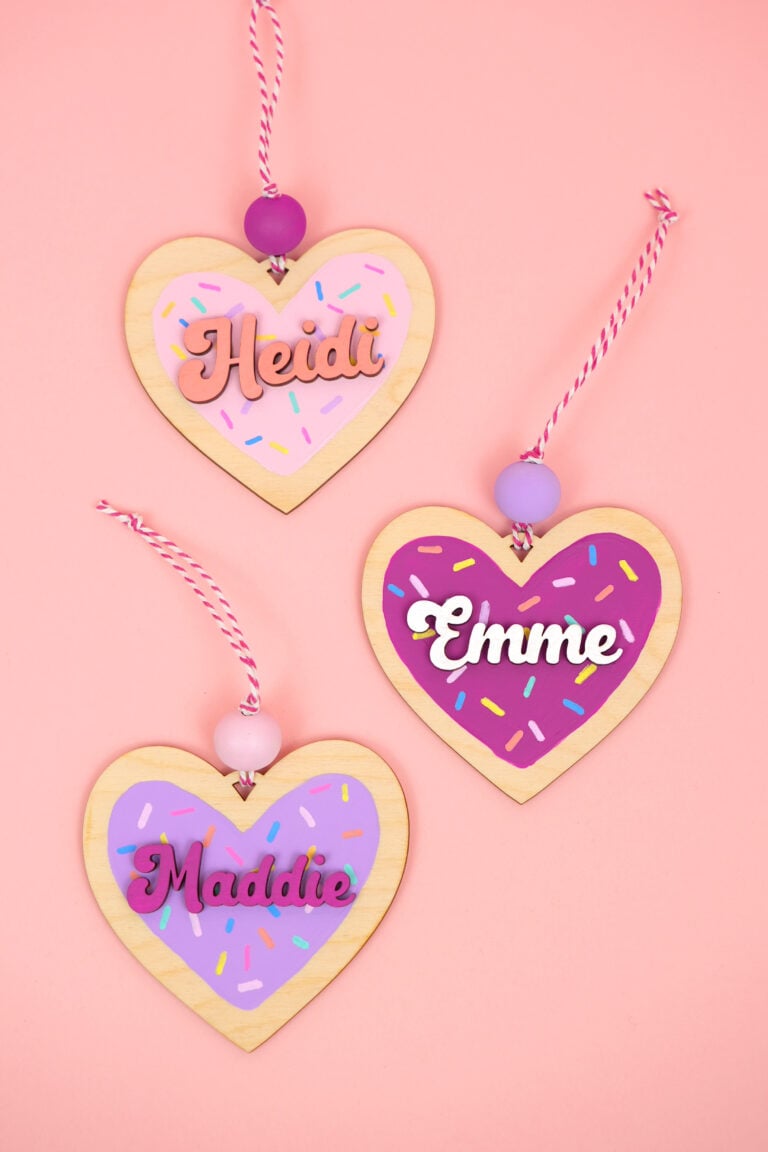 Three cute heart "cookie" ornaments cut from wood and painted on a pink background