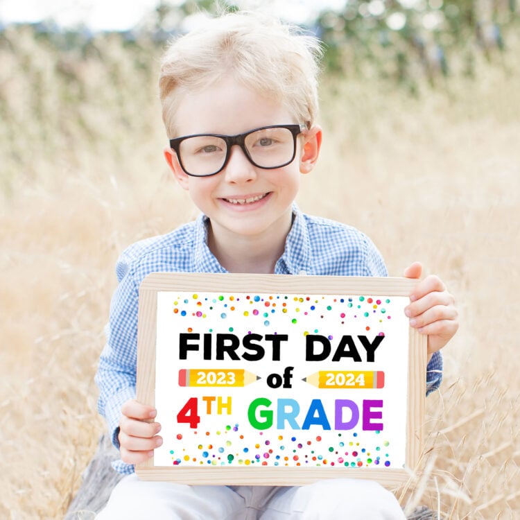 smiling schoolboy in glasses holding "first day of school" sign in the park