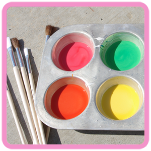Colorful sidewalk chalk paint in tray with paintbrushes on concrete