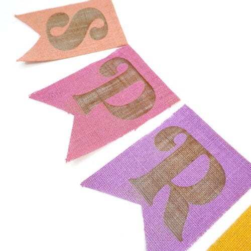 Close up of colorful "Hello Spring" laser engraved burlap banner pieces on a white background