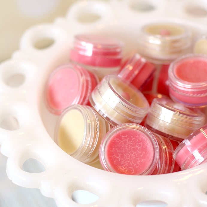 Close up of pink and natural colored lip balm in small plastic containers inside a vintage white bowl