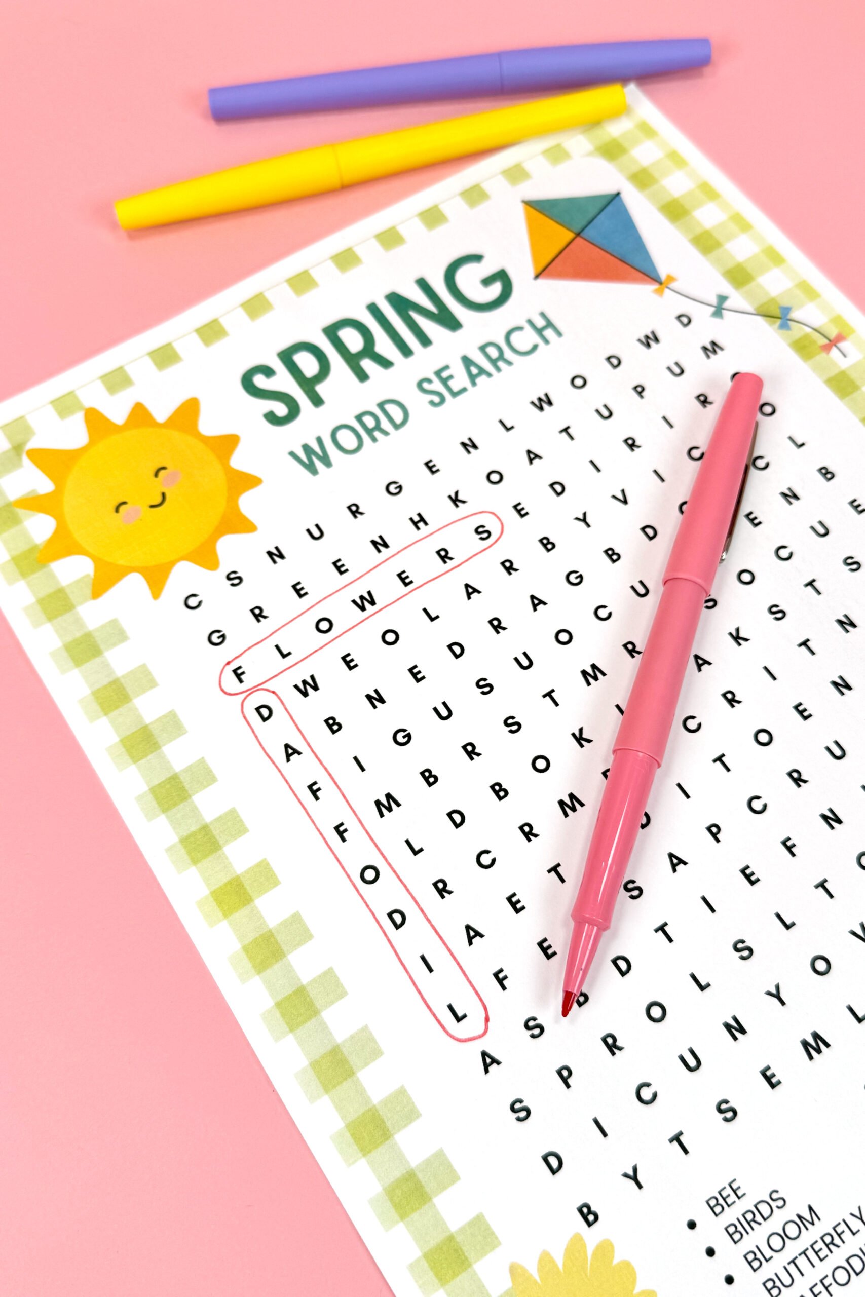 Close-up of printable spring word search with circled words on pink background with colorful pens
