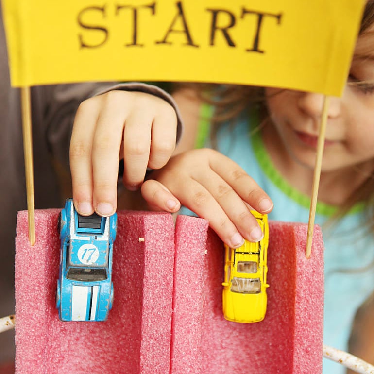 Close up of little hands with matchbox cars on a red pool noodle race track