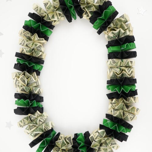 DIY graduation money lei on a white background with dollar bills and green and black rosettes