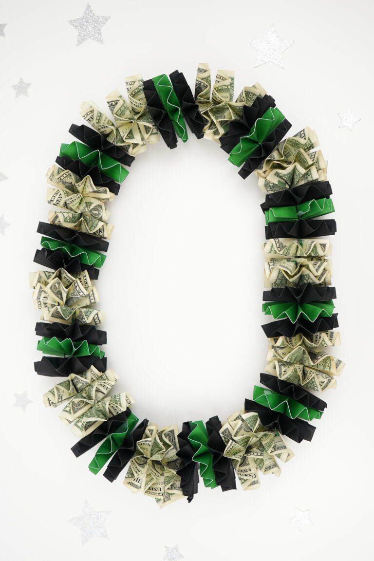 DIY graduation money lei on a white background with dollar bills and green and black rosettes