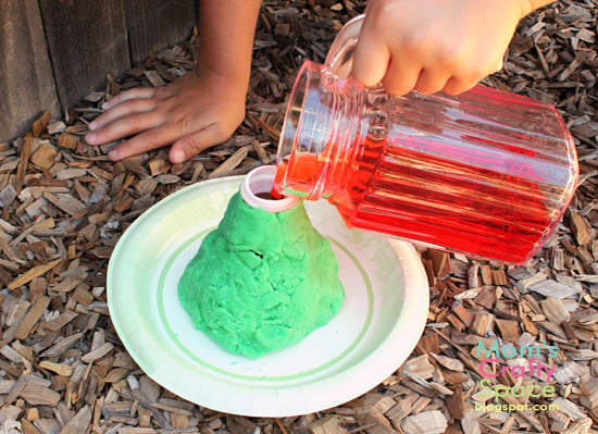 child pouring liquid into volcano science experiment 