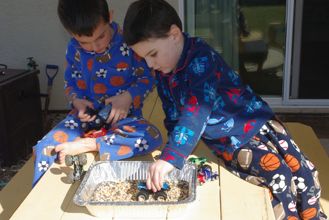 kids driving toy cars over bird seed in tray