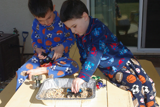 kids driving toy cars over bird seed in tray