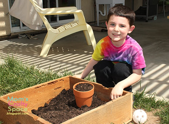 child placing pot full of soil into planter