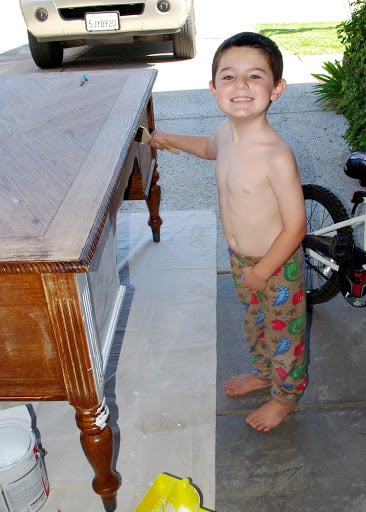 boy smiling with paint brush on sanded desk