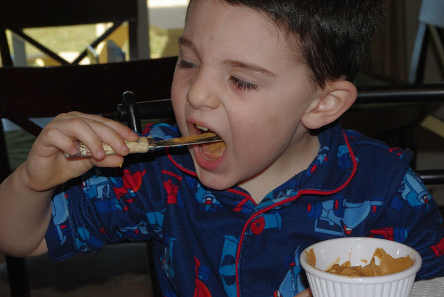 little boy eating peanut butter off of knife