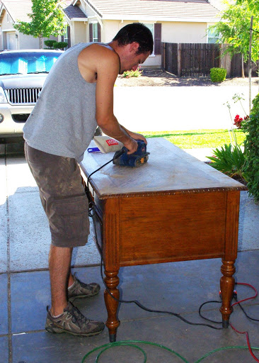 man sanding old desk down in driveway