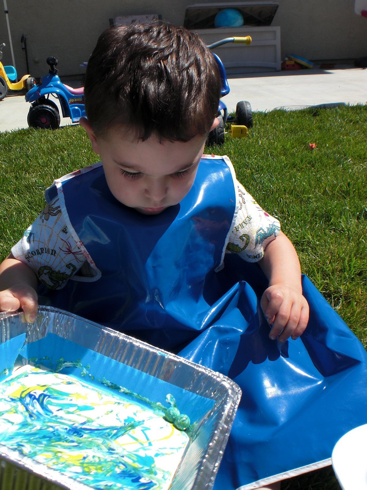 small child wearing apron painting with marbles in tray